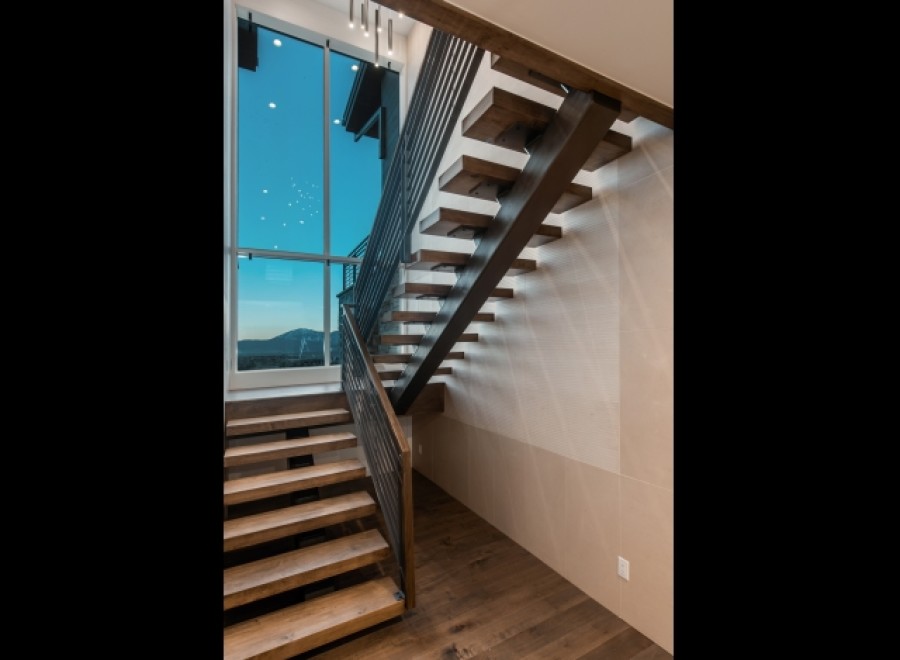 Modern staircase with sleek metal railing and rich wood treads, offering a stunning view through a large window.
