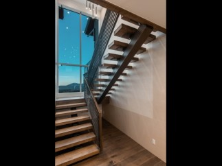 Modern staircase with sleek metal railing and rich wood treads, offering a stunning view through a large window.