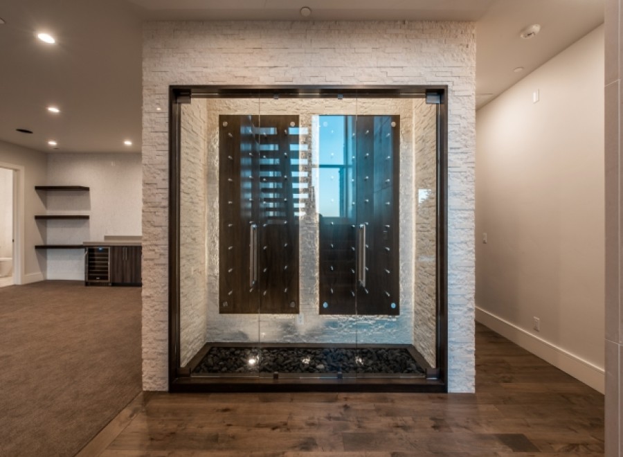 This stunning home boasts a custom-built wine cellar, showcasing a sleek, modern design with glass doors and a unique stone feature wall.