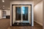 This stunning home boasts a custom-built wine cellar, showcasing a sleek, modern design with glass doors and a unique stone feature wall.