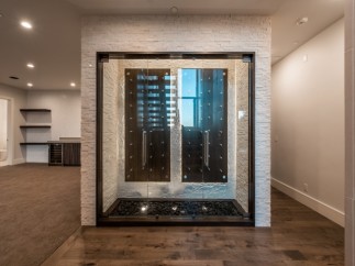 This stunning home boasts a custom-built wine cellar, showcasing a sleek, modern design with glass doors and a unique stone feature wall.