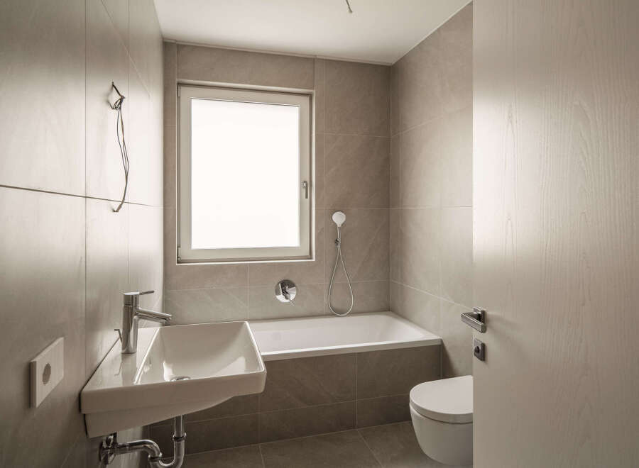 This modern bathroom features a sleek white sink with chrome fixtures, a spacious bathtub, and a wall-mounted toilet.
