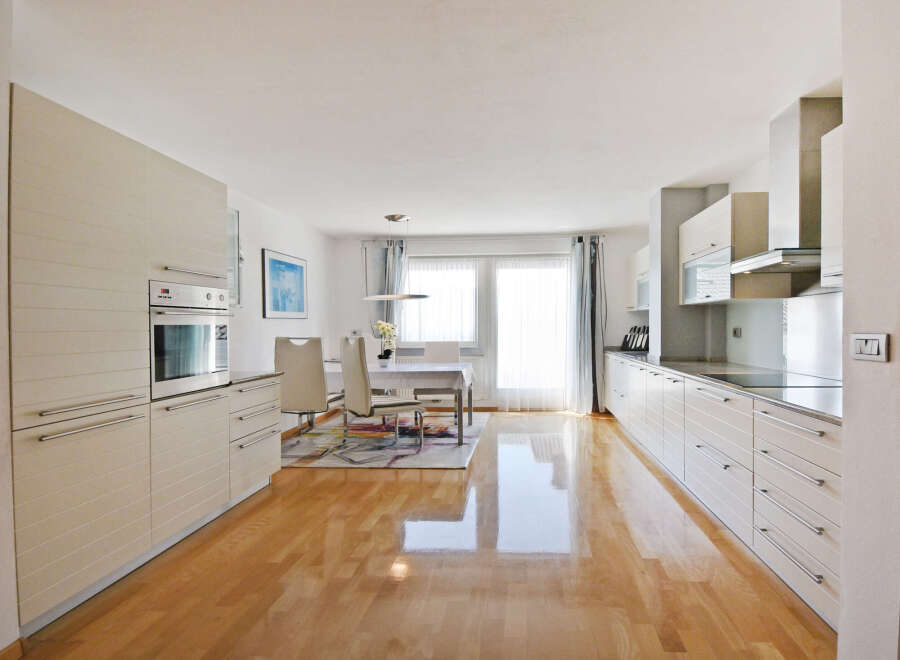 Experience modern living in this spacious kitchen and dining area, featuring sleek white cabinetry and a built-in oven.