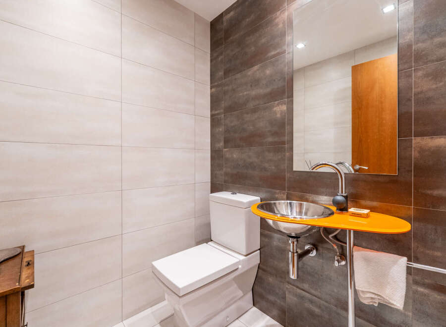 This modern bathroom features a unique design with a sleek, orange sink and a stylish mirror.