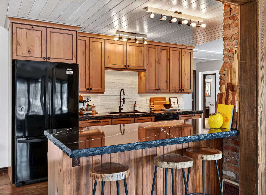 This stunning kitchen boasts custom wooden cabinetry, a sleek black countertop, and a stylish breakfast bar.