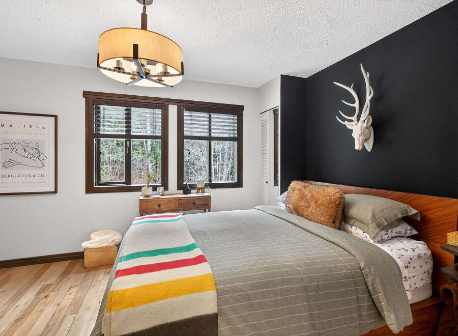 Step into a cozy bedroom retreat! This space features a stylish bed, a striking black accent wall adorned with a unique deer head, and a charming window that brings in natural light.