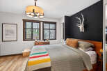 Step into a cozy bedroom retreat! This space features a stylish bed, a striking black accent wall adorned with a unique deer head, and a charming window that brings in natural light.