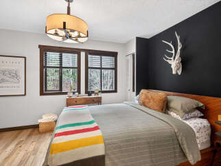 Step into a cozy bedroom retreat! This space features a stylish bed, a striking black accent wall adorned with a unique deer head, and a charming window that brings in natural light.