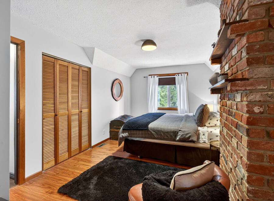 This cozy bedroom features a rustic brick accent wall and a charming wooden closet.