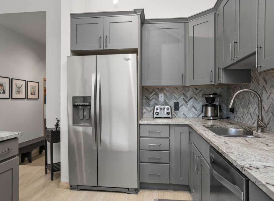 This stunning kitchen boasts modern gray cabinetry, complemented by a sleek stainless steel Whirlpool refrigerator.