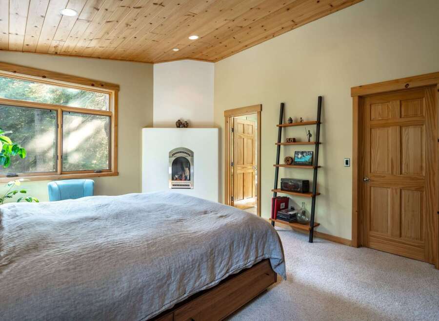 Experience cozy comfort in this inviting bedroom, featuring a charming fireplace and a large window offering serene views of nature.