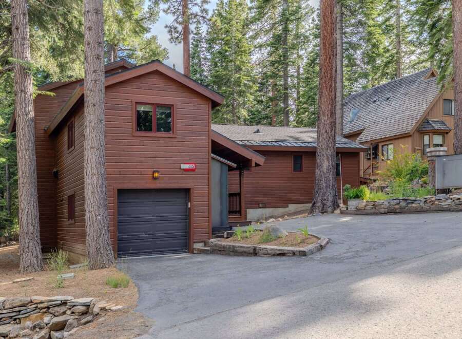 Nestled amongst towering pine trees, this charming property features a rustic wooden exterior and a convenient attached garage.