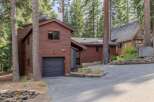 Nestled amongst towering pine trees, this charming property features a rustic wooden exterior and a convenient attached garage.