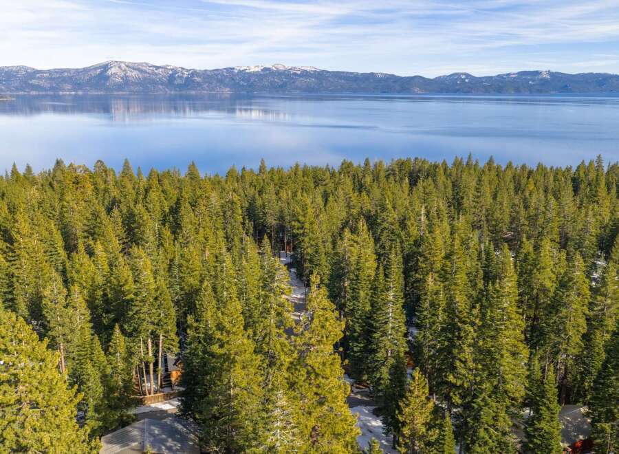 Nestled amidst a dense forest of evergreen trees, this property offers a serene retreat with stunning views of a vast, calm lake and snow-capped mountains in the distance.