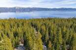 Nestled amidst a dense forest of evergreen trees, this property offers a serene retreat with stunning views of a vast, calm lake and snow-capped mountains in the distance.