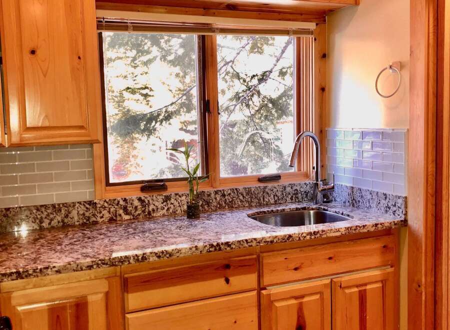This charming kitchen features beautiful light wood cabinetry, complemented by a speckled granite countertop and a light blue subway tile backsplash.