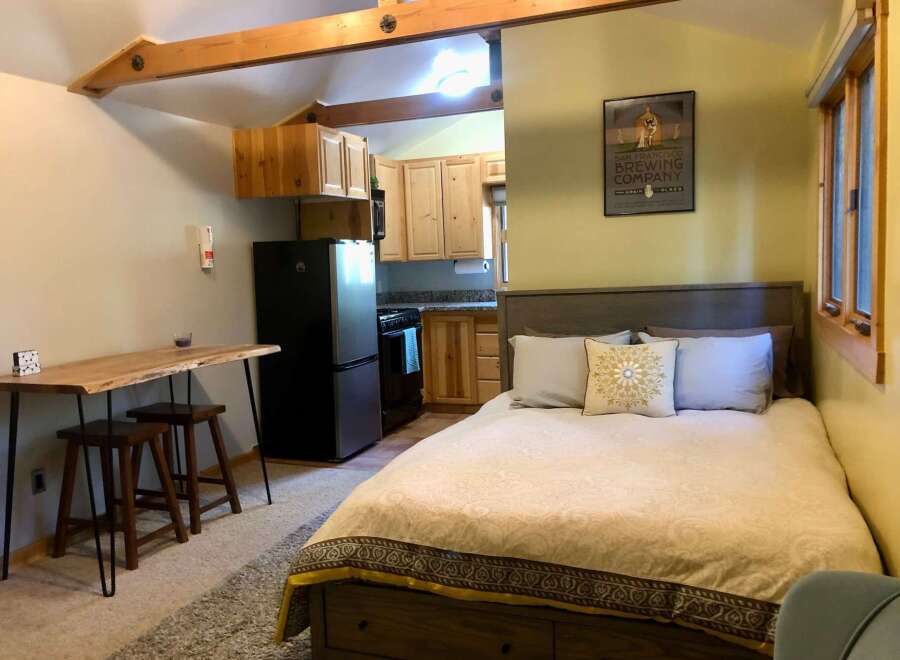 Discover this charming studio apartment featuring a cozy sleeping area with a comfortable bed and decorative pillows.