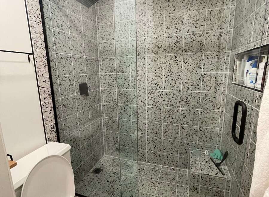 Step into a modern bathroom oasis! This stunning space features a sleek glass shower enclosure with a rainfall showerhead, complemented by stylish terrazzo tile.