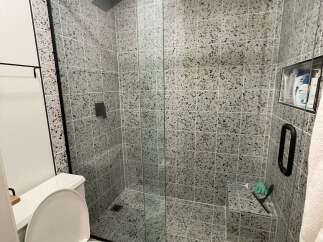 Step into a modern bathroom oasis! This stunning space features a sleek glass shower enclosure with a rainfall showerhead, complemented by stylish terrazzo tile.