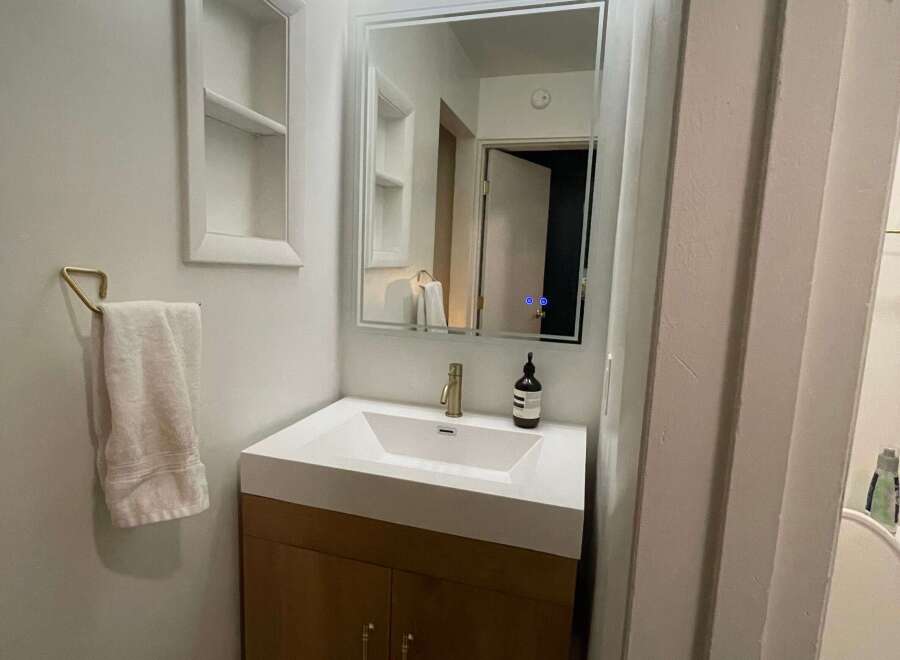 This modern bathroom features a sleek vanity with a white countertop and wooden cabinets, offering ample storage space.
