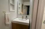 This modern bathroom features a sleek vanity with a white countertop and wooden cabinets, offering ample storage space.