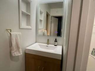 This modern bathroom features a sleek vanity with a white countertop and wooden cabinets, offering ample storage space.