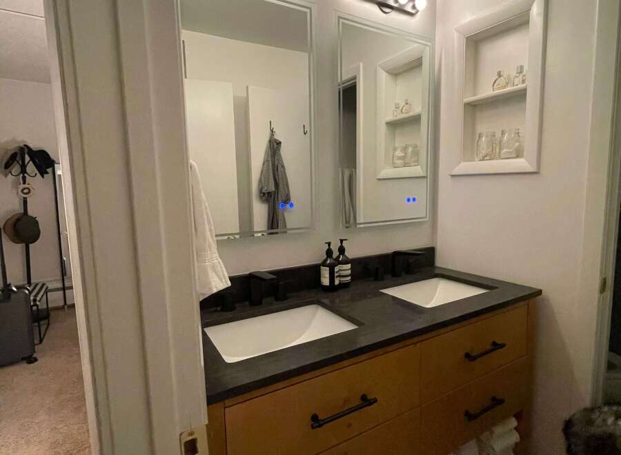 This modern bathroom features a sleek double vanity with a dark countertop and wooden cabinets, offering ample storage space.