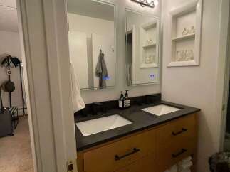 This modern bathroom features a sleek double vanity with a dark countertop and wooden cabinets, offering ample storage space.