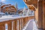 Experience the charm of a winter wonderland from this stunning wooden balcony, offering breathtaking views of snow-covered chalets and majestic pine trees.