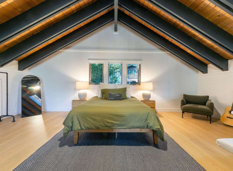 This stunning bedroom boasts a unique architectural design with exposed wooden beams and a vaulted ceiling, creating a spacious and airy feel.