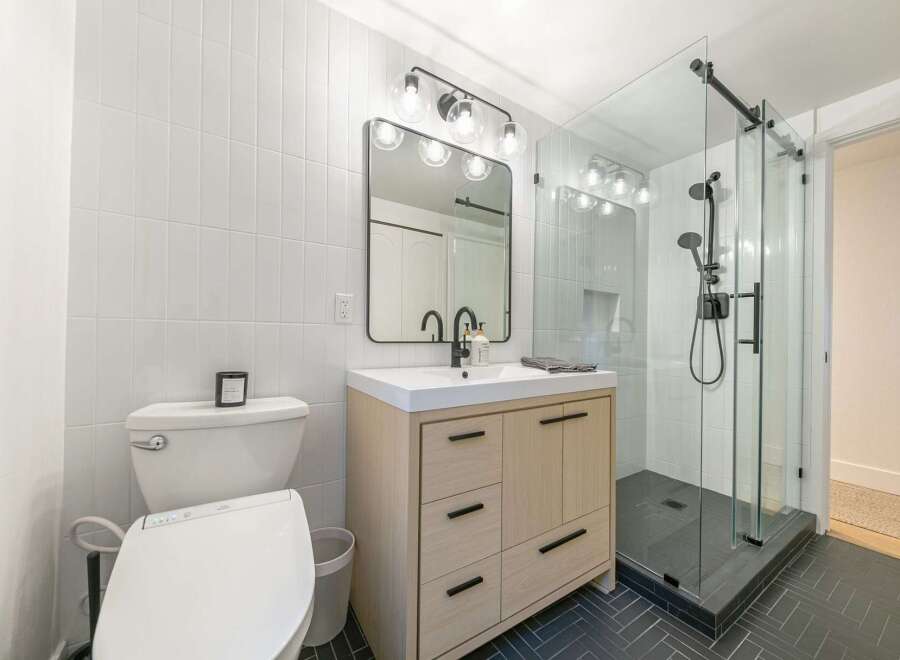 Step into a modern bathroom oasis! This stunning space features sleek white tile, a stylish vanity, and a luxurious glass shower.