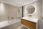 This modern bathroom features a sleek design with a floating vanity and a round, illuminated mirror.