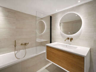 This modern bathroom features a sleek design with a floating vanity and a round, illuminated mirror.