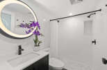 Step into a modern bathroom oasis! This stunning space features sleek white tiles, a stylish black vanity, and a beautiful round mirror with integrated lighting.