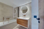 This modern bathroom boasts a sleek design with a wooden vanity and a round mirror with integrated lighting.