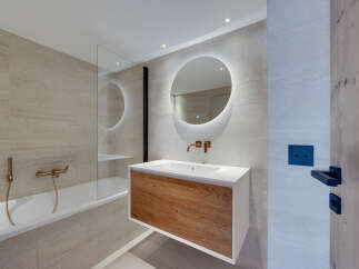 This modern bathroom boasts a sleek design with a wooden vanity and a round mirror with integrated lighting.