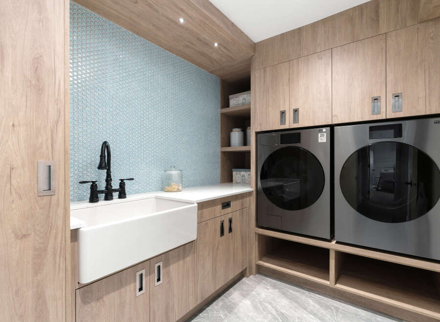 This stunning laundry room boasts a modern design with sleek cabinetry and a beautiful blue tile backsplash.