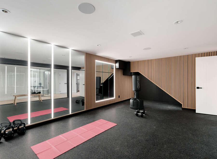 This modern home gym features a sleek design with a large mirror wall and integrated lighting, creating an open and inviting space.
