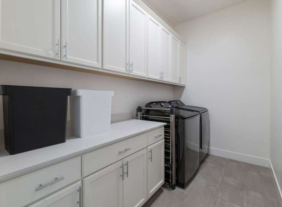 This stunning laundry room boasts ample storage with its sleek white cabinets and a pristine countertop.