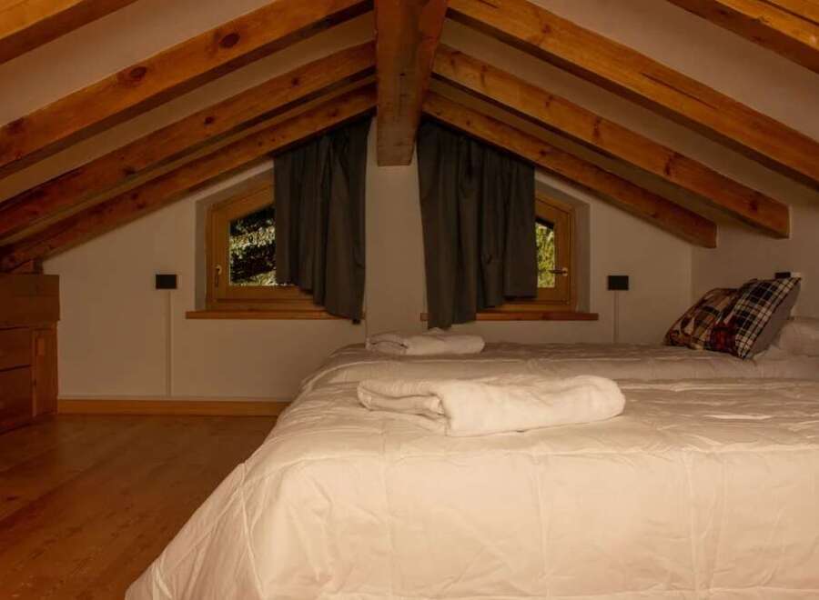 This cozy attic bedroom features a charming wooden beamed ceiling and a comfortable bed, perfect for a relaxing getaway.