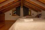 This cozy attic bedroom features a charming wooden beamed ceiling and a comfortable bed, perfect for a relaxing getaway.
