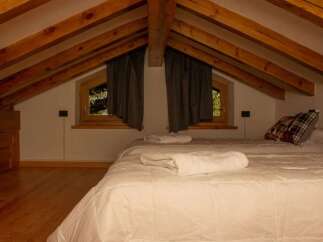 This cozy attic bedroom features a charming wooden beamed ceiling and a comfortable bed, perfect for a relaxing getaway.