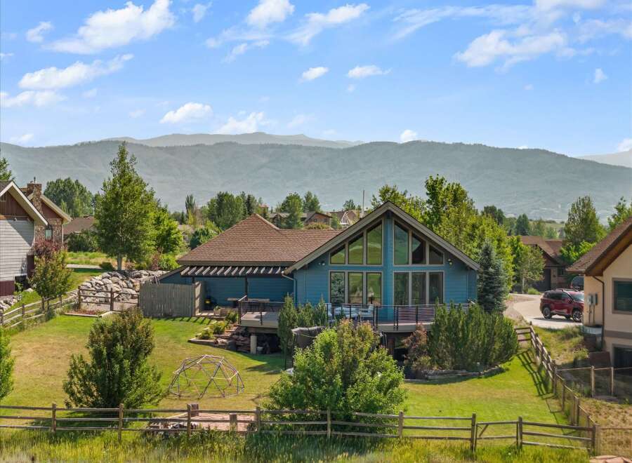 Experience breathtaking mountain views from this stunning blue home, featuring a spacious deck perfect for entertaining and large windows that flood the interior with natural light.