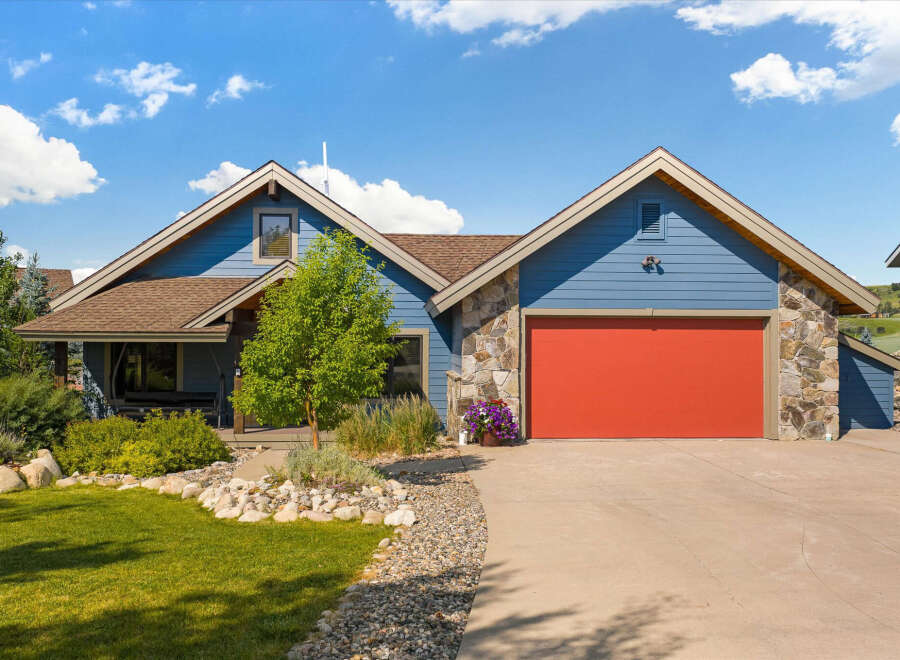 Charming blue siding home featuring a vibrant red garage door and natural stone accents.