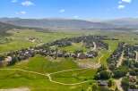 Discover this stunning aerial view of a picturesque suburban neighborhood nestled amidst rolling green hills and majestic mountains.