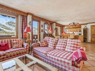 Experience the charm of this cozy chalet, featuring a spacious living area with a comfortable plaid sofa and stunning mountain views.