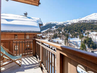 Enjoy breathtaking mountain views from this charming wooden balcony, complete with a comfortable lounge chair perfect for soaking in the alpine scenery.