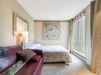 This cozy bedroom features a comfortable bed with a patterned quilt and a stylish red leather sofa, perfect for relaxing.