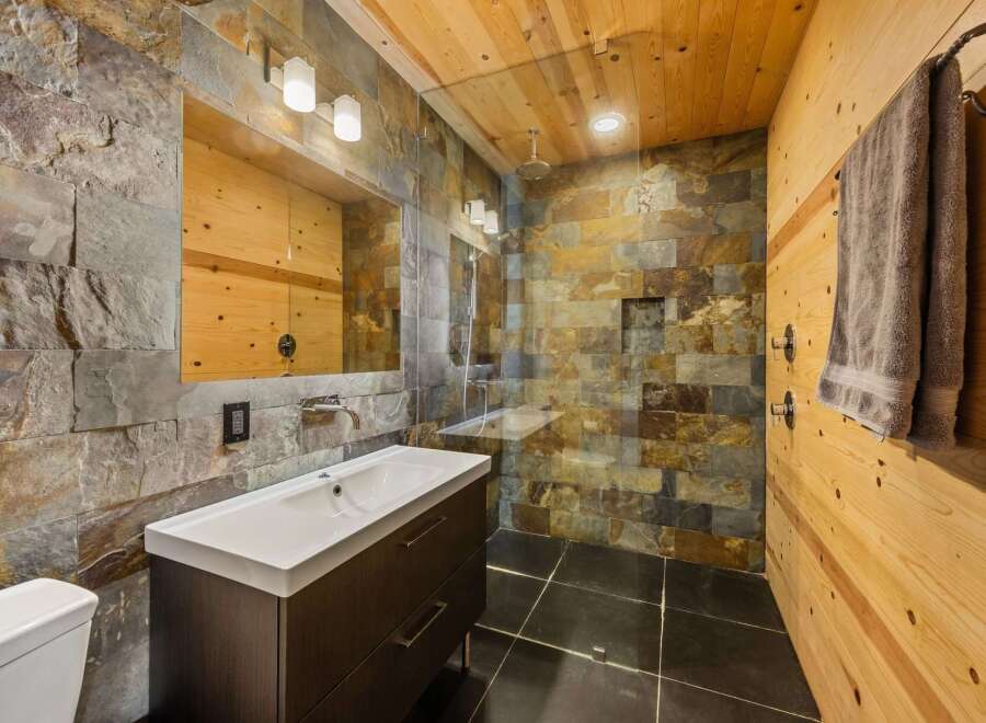 Step into luxury with this stunning bathroom featuring a unique stone tile shower and a sleek, modern vanity.