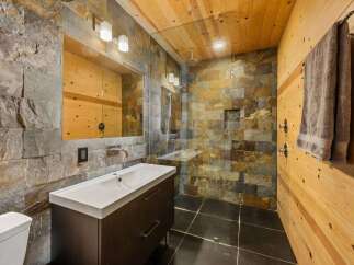 Step into luxury with this stunning bathroom featuring a unique stone tile shower and a sleek, modern vanity.